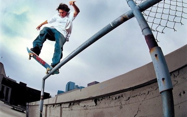 Un joven sobre una patineta la cual está equilibrando sobre una baranda
