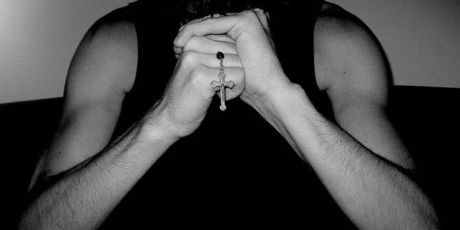 Una persona sin su cara visible sostiene un crucifijo en sus manos