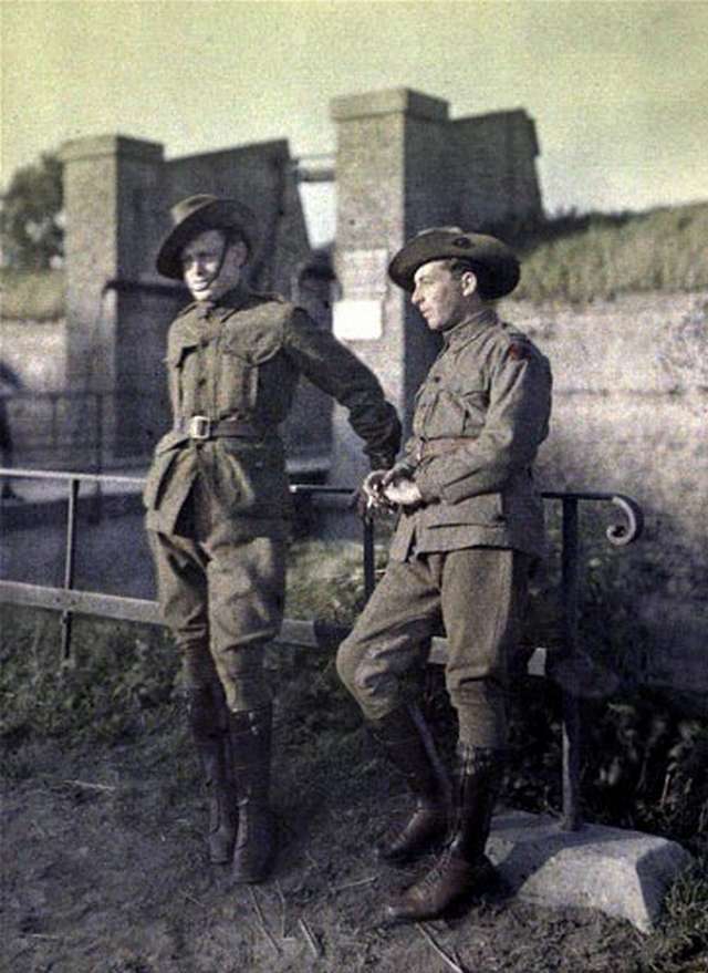 Vemos a dos soldados que sonríen  al frente de un edificio tienen sombreros con  correa en la barbilla