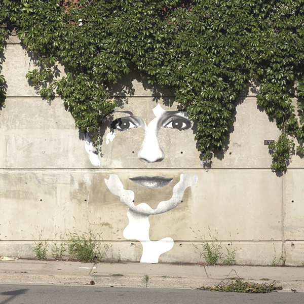 Vemos un rostro de mujer pintado en una pared de la parte alta de la pared baja un ramo de hojas que se ve como pelo