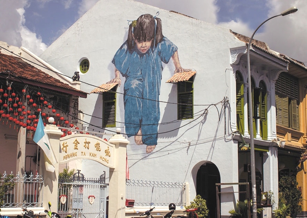 Vemos  unas lindas casas con rejas plantas y sobre una pared una niña pintada que trata de sostenerse sobre una cuerda de la luz