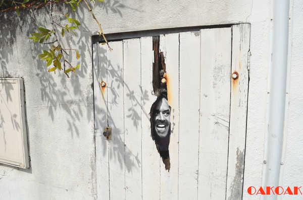 Hay una vieja puerta en madera blanca donde aparece el rostro de un hombrere joven sonriendo y da un aspecto que alguien estuviera alli 