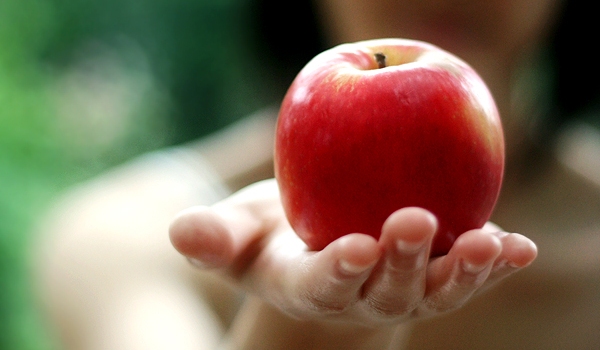 Vemos a una mano que sostiene una hermosa manzana muy roja 