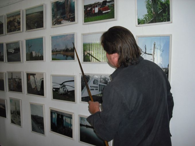 Vemos un hombre con una regla en la mano y sobre la pared donde hay muchas fotos que el Sr señala