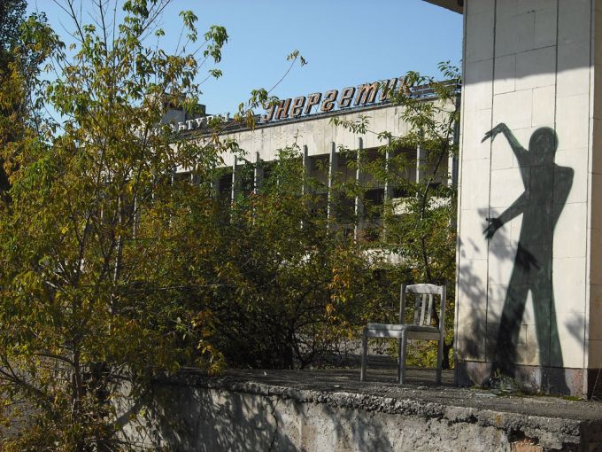 Tenemos una pared donde vemos un graffiti de una figura en negro tambien sillas desun poco destruidas y tambien abundante vegetacion