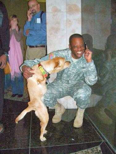 Tenemos a varias personas aqui y uh hombre con uniforme militar que habla por celular y abraz a al perro 