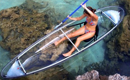 Tenemos una mujer en bikini que rema desde una  canoa transparente que permite ver el fondo