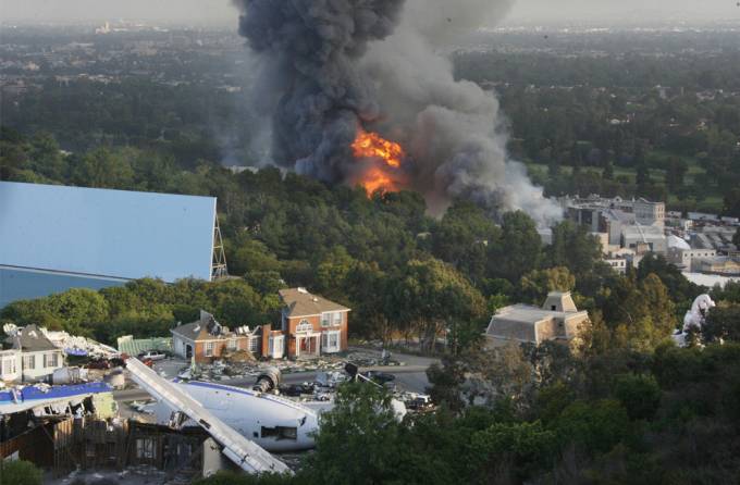 Vemos un incendio que ocurre en medio de unas casa y también se ve un avión mientras las llamas se observan muy altas