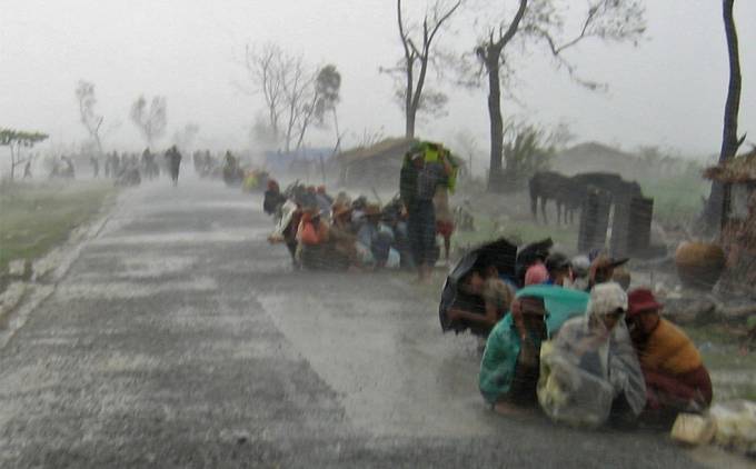 Tenemos unas personas sentadas en el suelo y cubiertas con plásticos y ponchos mientras llueve torrecialmente