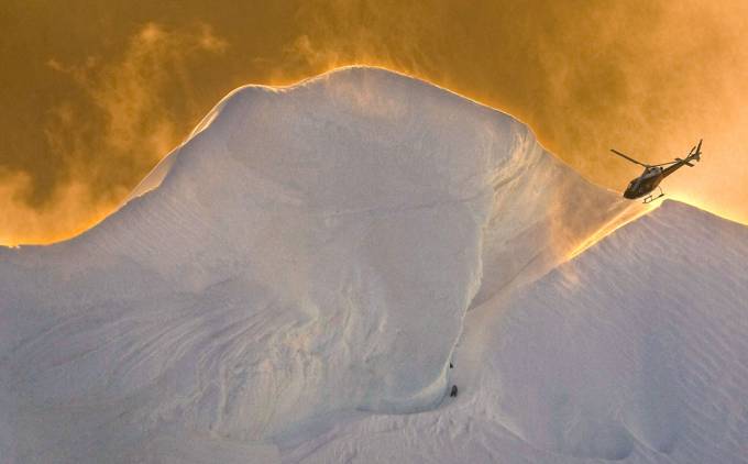 Vemos una cumbre nevada y entre la nieve vemos aun hombre que espera al helicóptero que se acerca a recogerlo