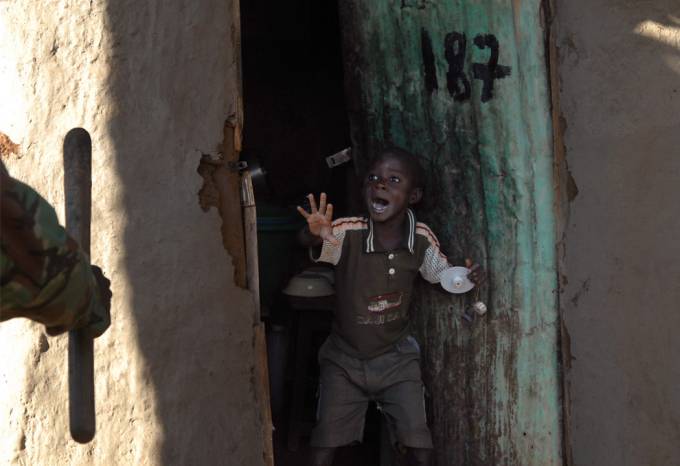 Un niño africano muestra cara de terror cuando al abrir la puerta de su casa ve aun policía con un arma en su mano