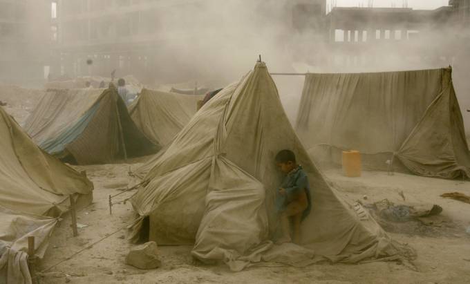 Un niño se esconde detrás de una carpa en el desierto mientras pasa una tormenta de arena