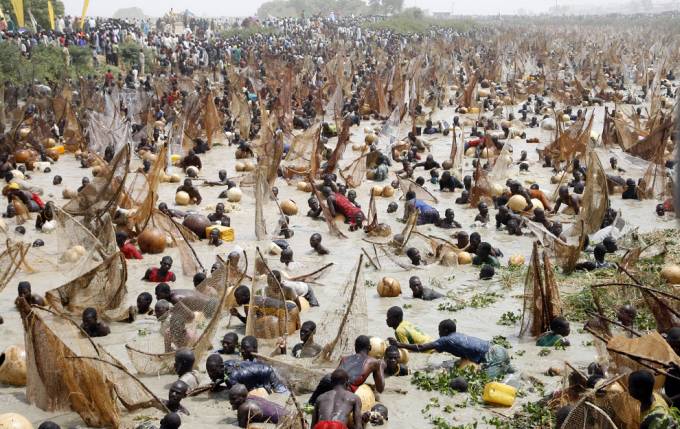 Miles de personas de color con redes en sus manos tratan de pescar en el rio que se ve