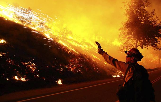 Un bombero lo vemos que lanza algo al frente se ve un color naranja de las llamas del incendio que se a lo,lejos