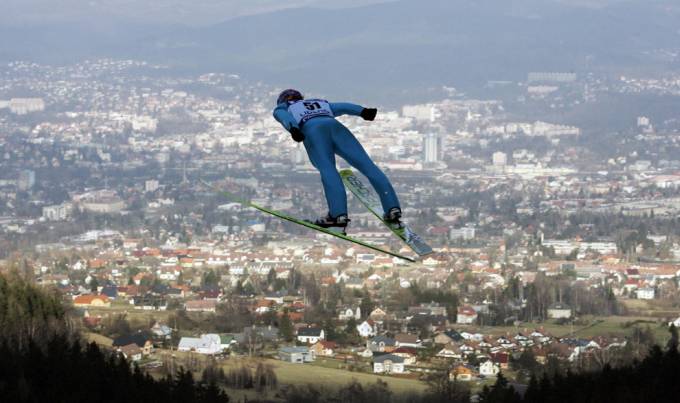 Un hombre con ski hace un salto largo de donde se ve una ciudad al fondo