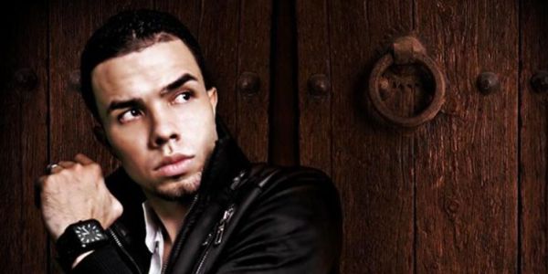 Un hombre joven con pelo oscuro con chaqueta negra en cuero parado delante de una puerta