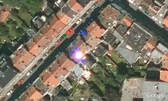 Tenemos un conglomerado de casas  muy iguales y una avenida que pasa y un reflejo de luz amarillo sobre el tejado de una casa 