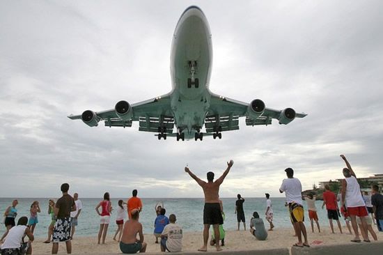 Vemos a un avion a muy baja altura y las personas en la playa lo saludan levantando sus brazos