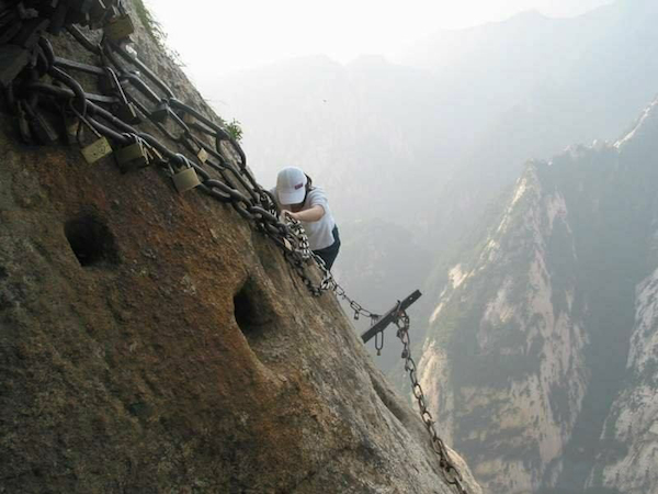 Tenemos una mujer que baja por la pared de la montaña ayudada por llas cadenas y apoyada en los tablones