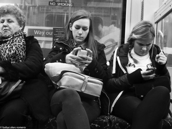 Tres mujeres sentadas dos jóvenes y una mayor miran sus celulares tranquilamente al fondo se observa una calle