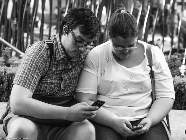 Una pareja el y ella observa cada uno su celular cómodamente al fondo se ve arboles