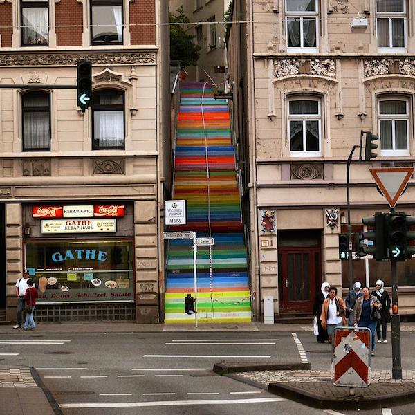 Vemos una escala en medio de dos edificios pintada en alegrs colores se ve tambien una calle  con varios carriles