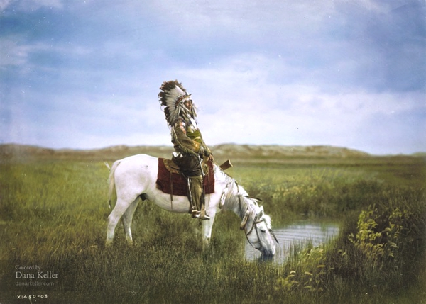 Tenemos a un jefe indio con su tocado de plumas en su cabeza va en un caballo blanco que toma agua en un riachuelo