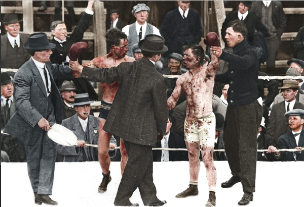 Vemos unos hombres con trajes y sombreros en un ring de boxeo un juez levanta la mano del ganador