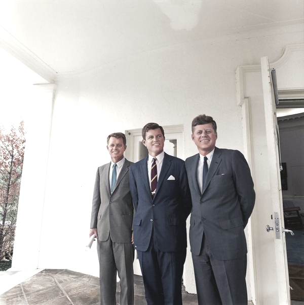 Observamos a tres hombres sonrientes con trajes y corbatas en un pasillo de un edificio 