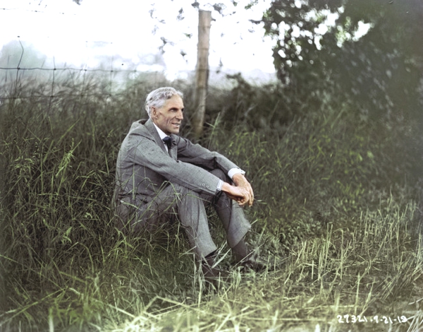 Vemos a un hombre mayor con traje y corbata sentado en un prado sonríe amigablemente