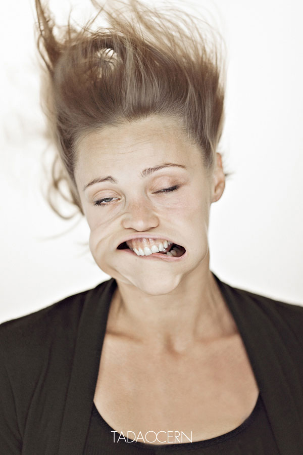 Una mujer rubia su pelo hacia arriba un solo ojo entreabierto y el otro casi cerrado su boca  torcida hacia un lado muestra los dientes sobre su labio inferior