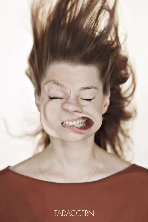 Una mujer con el pelo hacia arriba y los ojos cerrados  y la boca hace una mueca hacia un lado mostrando los dientes y su encia 