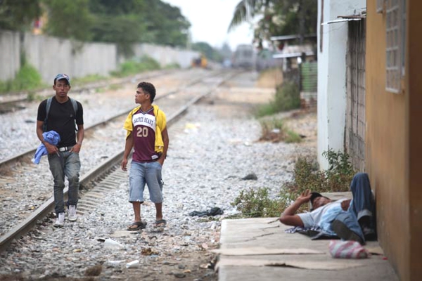 Ahora vemos a dos hombres muy jóvenes que caminan al lado de la carrilera del tren y otro que descansa acostado en el piso