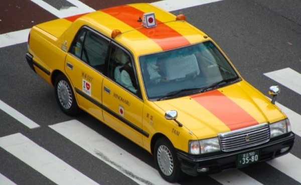 Vemos un taxi amarillo con franjas naranjas  que se desplaza por una ciudad