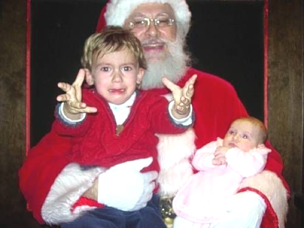 Una niña de brazos y un niño mas grandes estan sentados en las piernas de Santa Claus y lloran amargamente