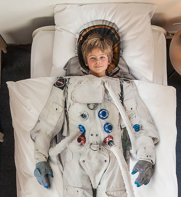 Observamos un edredón blanco con una figura de un astronauta y debajo un niño rubio que parece que tuviera puesto el traje de astronauta