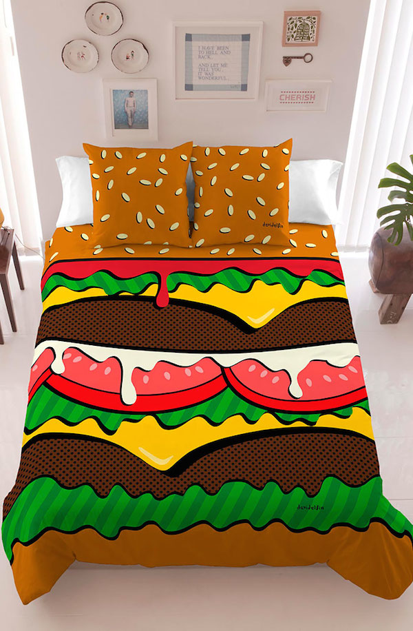 Vemos un hermoso tendido con colores muy fuertes y almohadas con semillas esparcidas  es la figura de una gran hamburguesa en  la pared hay platos de adorno