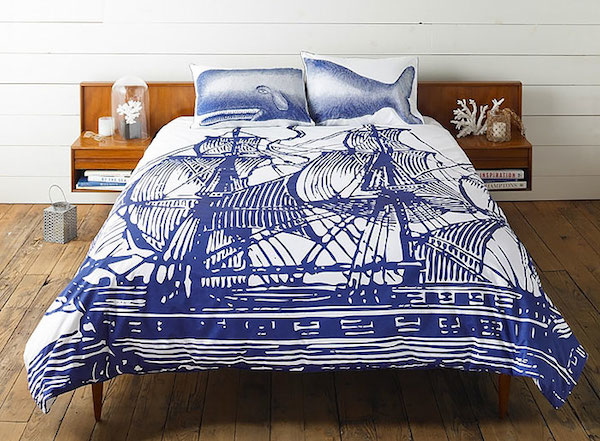Observamos una cama amplia con un tendido donde hay dos grandes veleros en color azul y las dos almohadas al juntarles forman un simpático cachalote 