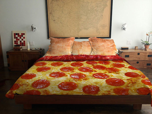 Vemos un edredon con grandes pizzas con carne y también  hay mesas con  varios objetos y mapa arriba de los cojines de la cama