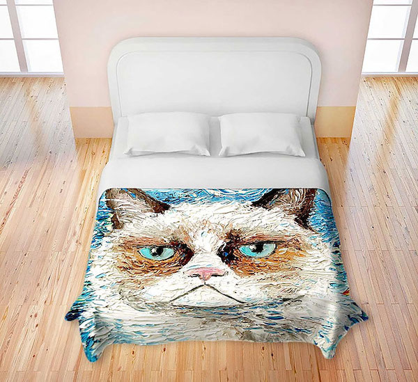 Observamos una cama tendida con sabanas y almohadas en blanco pero en la parte de abajo hay un  pequeño tendio con la figura en azul de un bello gato