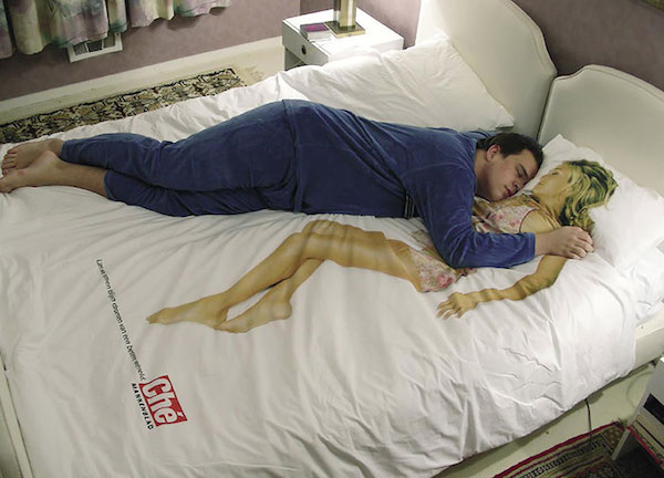 Vemos sobre una cama grande a un hombre en pijama azul abrazando una mujer que esta dibujada en la sabana  que tiene puesta la cama